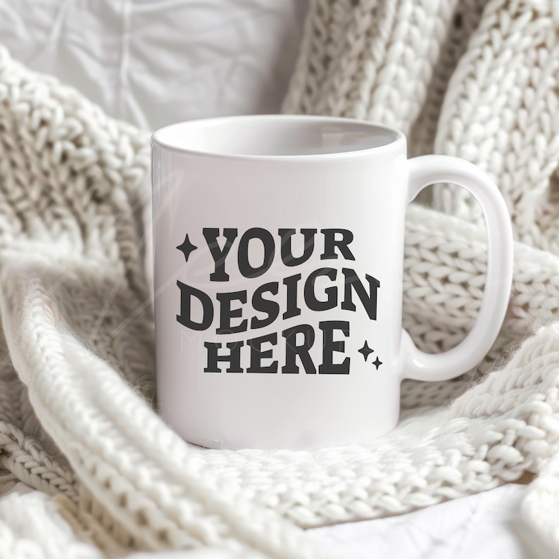 May include: White ceramic mug with a black design that says "YOUR DESIGN HERE" surrounded by small stars. The mug is sitting on a white knitted blanket.