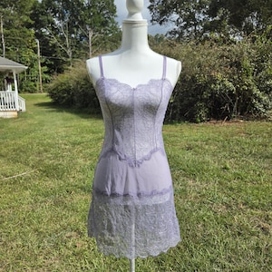May include: A lavender slip dress featuring a sweetheart neckline with thin shoulder straps. The bodice is crafted from floral lace, transitioning into a smooth fabric midsection, and finished with a wide, scalloped lace hemline at the bottom.