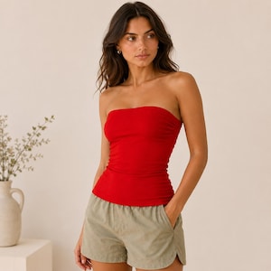Pode incluir: Um top de tubo vermelho vibrante sem alças combinado com calções verde-azeitona claro. A parte superior apresenta um decote reto e justo e um tecido liso de cor sólida. Os calções têm um ajuste relaxado com bolsos laterais.