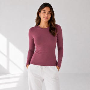 May include: A long-sleeve crew neck shirt in a solid dark mauve color. The shirt features a fitted silhouette with long sleeves and a standard round neckline. The fabric appears to be a smooth, opaque knit material, providing a clean and simple look.