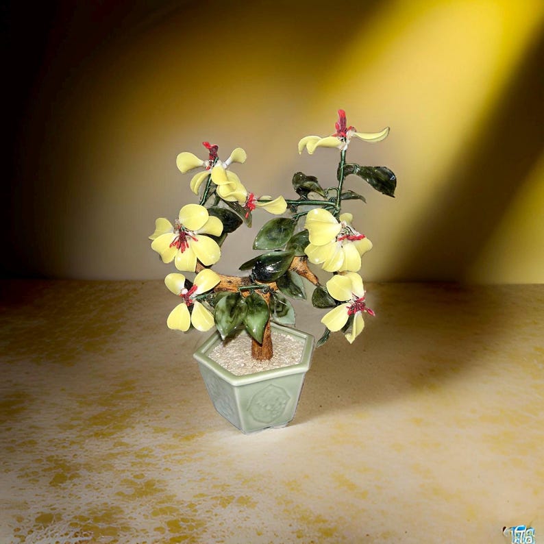May include: A jade bonsai tree with yellow flowers in a green ceramic pot. The tree is made of green jade and the flowers are made of glass.