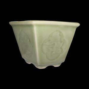 May include: A light green ceramic planter with a square shape and a scalloped rim. The planter has a raised design of stylized flowers on each side.