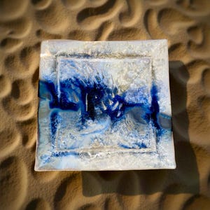 May include: A square glass tray with a raised, textured border. The tray has a blue and white design with a swirling pattern.