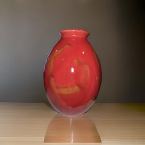 May include: A red ceramic vase with a rounded shape and a glossy finish. The vase has a subtle marbled pattern in a lighter shade of red.
