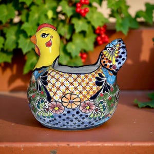 May include: A hand-painted ceramic hen-shaped planter. The planter features a yellow head with a red comb and a colorful body with floral and geometric patterns. The base is blue with white dots. The hen is approximately 8 inches long.