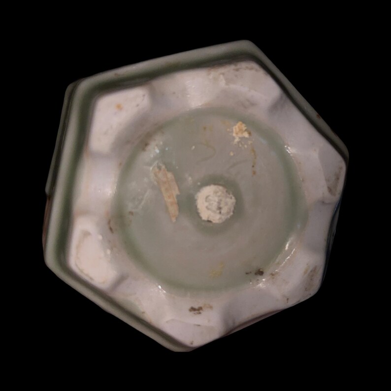 May include: The bottom of an octagonal ceramic planter with a green glaze. The planter has a white interior and a small hole in the center.