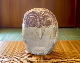 May include: A ceramic owl figurine with brown and white glaze. The owl has closed eyes and a beak.