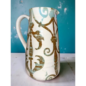 May include: A white ceramic pitcher with a brown and blue floral pattern. The pitcher has a wide mouth and a handle.