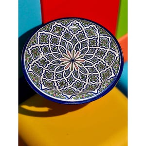 May include: A large, round ceramic plate with a blue rim and intricate geometric patterns in shades of green, blue, and pink.