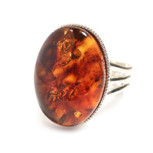 Peut inclure: Une bague en argent avec une pierre ovale en ambre. La pierre est de couleur brune et orange avec un motif marbré.