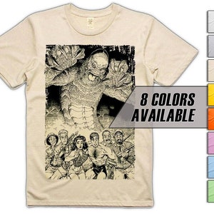 May include: A beige t-shirt featuring a black and white illustration of a creature from the black lagoon. The creature is standing over a group of people. The text "8 COLORS AVAILABLE" is in a white box on the right side of the image.