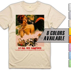 May include: A beige t-shirt featuring a vintage movie poster print of a vampire film called "Le Bal des Vampires". The poster depicts a woman with red hair and a vampire wearing a red cape. The text on the poster reads "The fearless vampire kills, in pardon me but your teeth are in my neck."