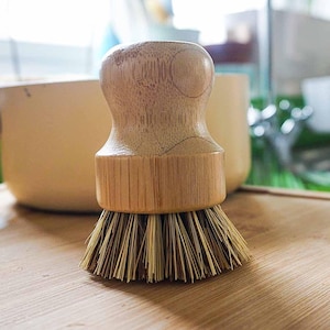 May include: A wooden dish brush with natural bristles. The brush has a round wooden handle with a slightly flared base.