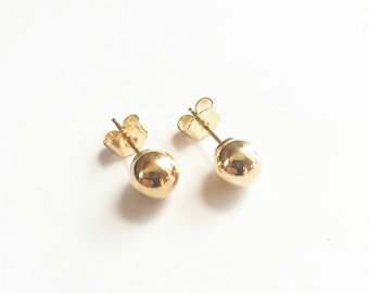 Può includere: Un paio di orecchini a lobo a forma di sfera dorata con una superficie liscia e riflettente. Ogni orecchino presenta un design sferico rotondo fissato a un perno sottile con una chiusura a farfalla dorata abbinata per il fissaggio.