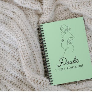 May include: A light green spiral bound notebook with a line drawing of a pregnant woman and the text "Doula I help people out".