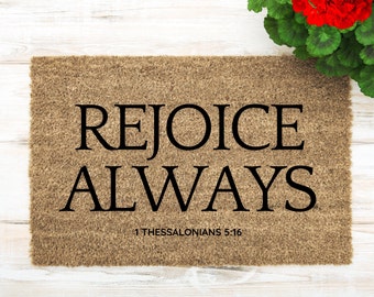 May include: A brown doormat with the text "REJOICE ALWAYS" in black lettering. The text "1 Thessalonians 5:16" is printed in smaller black lettering below the main text.