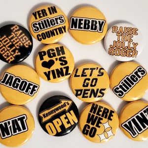 May include: A collection of 12 yellow and black round buttons with various Pittsburgh-themed slogans and graphics. The slogans include "Raise the Jolly Roger", "Let's Go Pens", "Here We Go", "N'at", "Jagoff", "Yer in Stillers Country", "Pgh 's Yinz", "Kennywood's Open", "Nebby", "Stillers", and "Vin".