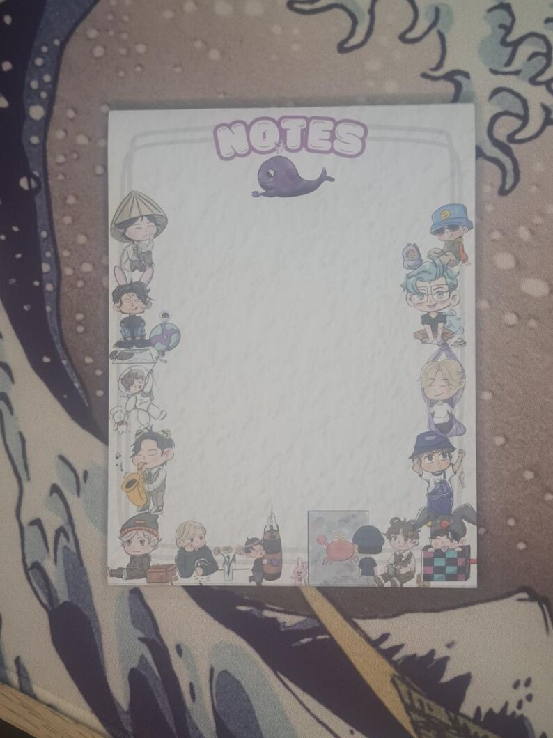 May include: A rectangular notepad featuring the word "NOTES" in purple bubble letters and a cartoon whale illustration. The notepad is bordered by cartoon figures in various outfits. The background is a blue and white patterned surface.