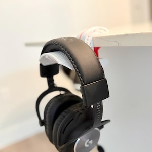 May include: Black over-ear headphones with a leather headband hanging on a white desk.