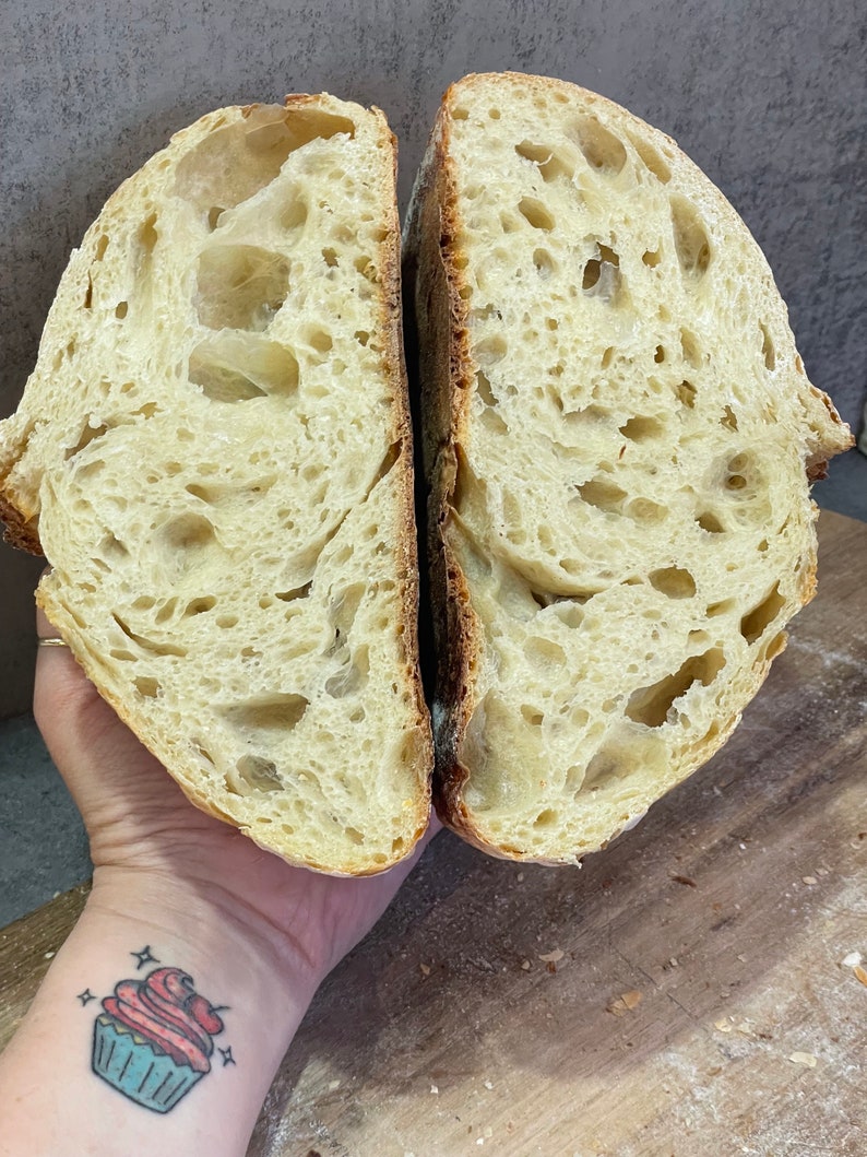 Photo of a baker holding a freshly baked sourdough loaf, sliced open to showcase the wild, airy crumb structure. Perfectly fermented bread with a golden crust, highlighting the art of homemade sourdough baking.