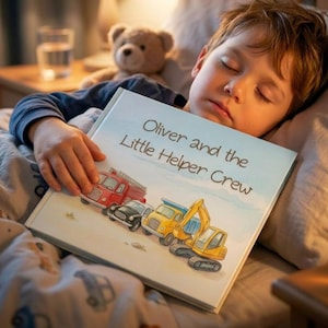 A little boy sleeping holding a book with the title, “Oliver and the Little Helper Crew”.
