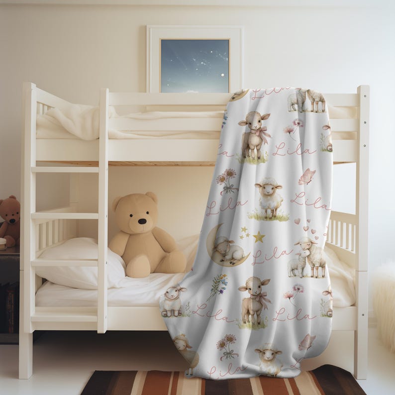 A personalized custom name white velveteen blanket with whimsical lambs, pink bows, stars, flowers, hearts and butterflies draped over a bunkbed.