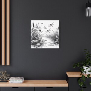 May include: Black and white canvas art print featuring a serene pond scene with dragonflies, lily pads, and reeds. The artwork is a detailed illustration, perfect for nature lovers and those seeking a calming aesthetic for their home decor.