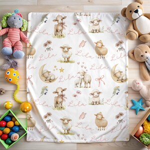 A personalized custom name white velveteen blanket with whimsical lambs, pink bows, stars, flowers, hearts and butterflies laying on the floor surrounded by toys.