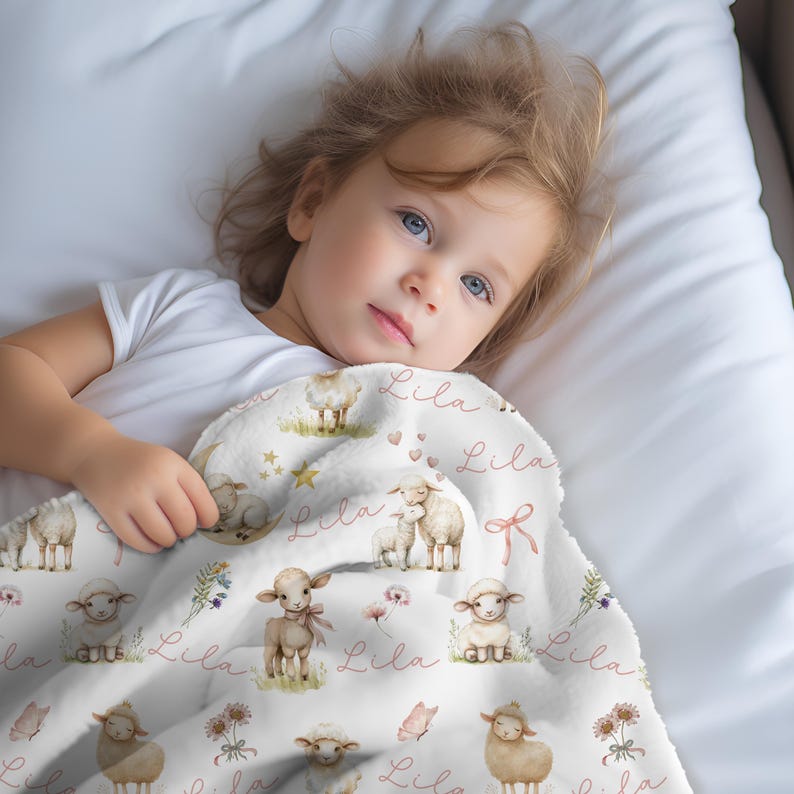 A little girl cuddled up with a personalized custom name white velveteen blanket with whimsical lambs, pink bows, stars, flowers, hearts and butterflies draped over a crib.