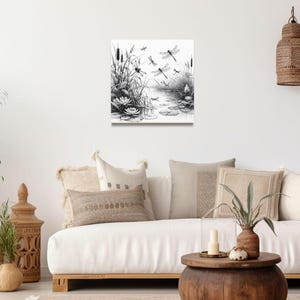Canvas wall art above a couch. The canvas wall art features an elegant black and white line art scene of dragonflies gracefully hovering over a tranquil pond.