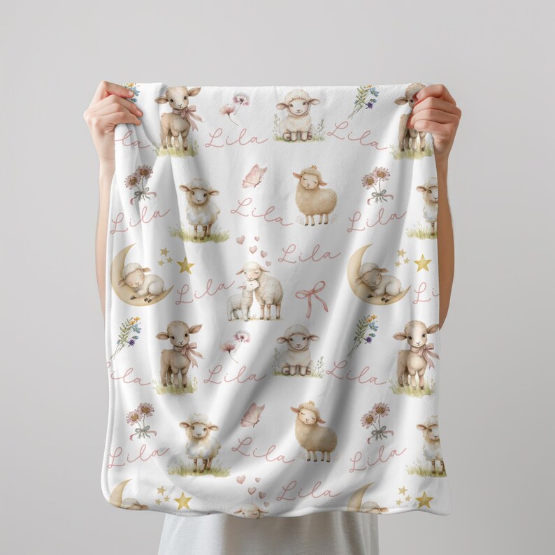 Two hands holding a  personalized custom name white velveteen blanket with whimsical lambs, pink bows, stars, flowers, hearts and butterflies.