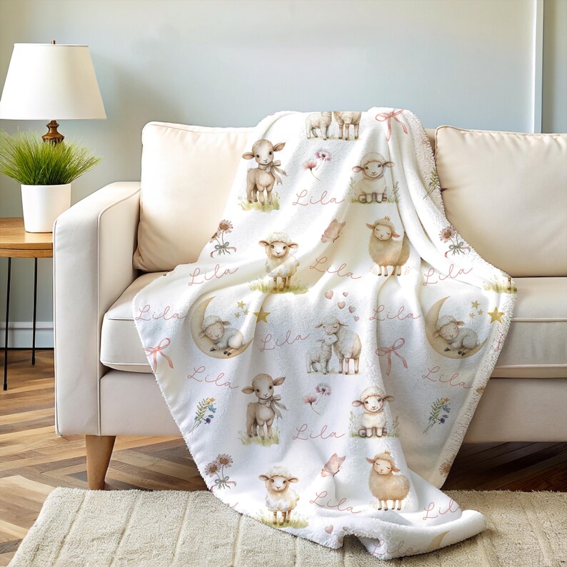 A personalized custom name white velveteen blanket with whimsical lambs, pink bows, stars, flowers, hearts and butterflies draped over a couch.