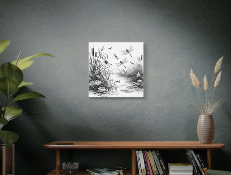 Wall canvas on a grey wall above a low bookcase. Canvas wall art is of elegant black and white line art scene of dragonflies gracefully hovering over a tranquil pond.