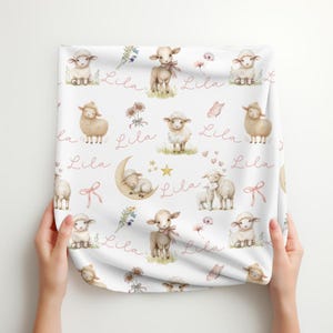 A folded personalized custom name white velveteen blanket with whimsical lambs, pink bows, stars, flowers, hearts and butterflies.