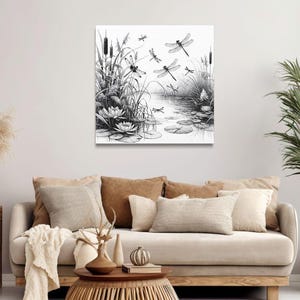Canvas wall art above a couch. The canvas wall art features an elegant black and white line art scene of dragonflies gracefully hovering over a tranquil pond.
