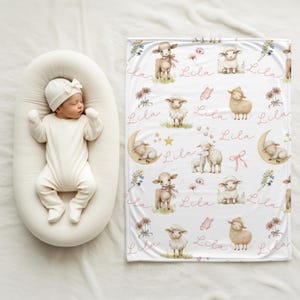A baby laying beside a personalized custom name white velveteen blanket with whimsical lambs, pink bows, stars, flowers, hearts and butterflies draped over a crib.