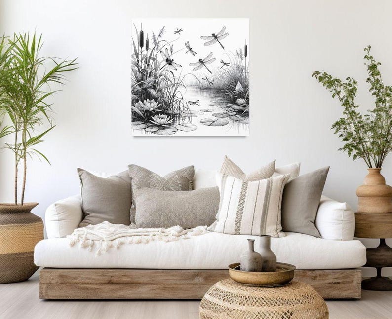 Canvas wall art above a couch with pillows. The canvas wall art features an elegant black and white line art scene of dragonflies gracefully hovering over a tranquil pond.