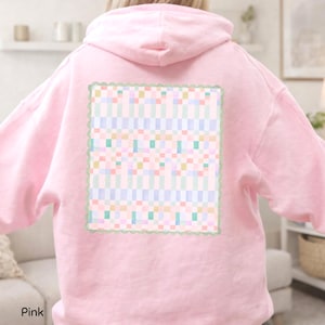 May include: A light pink hooded sweatshirt featuring a large rectangular graphic on the back. The graphic displays a multi-colored pixelated grid pattern in shades of blue, green, yellow, and pink, framed by a scalloped sage green border.