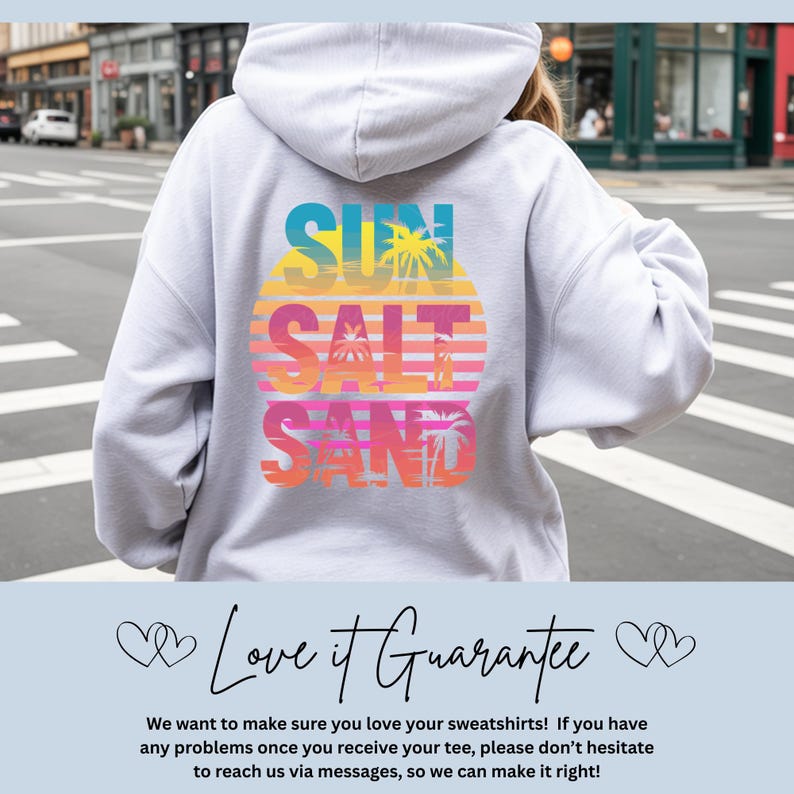 K&ouml;nnte beinhalten: Ein hellgrauer Kapuzenpullover mit einem Grafikdruck auf der R&uuml;ckseite, der den Text SUN SALT SAND &uuml;ber einem kreisf&ouml;rmigen Sonnenuntergangsmotiv in T&uuml;rkis, Gelb, Orange und Pink zeigt, erg&auml;nzt durch Palmensilhouetten und horizontale Linien.