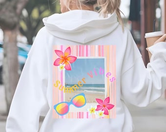 Puede incluir: Una sudadera con capucha blanca que presenta un gráfico en la parte posterior. El diseño incluye un marco rectangular que muestra una escena de playa, rodeado de rayas verticales rosas y naranjas, flores tropicales, gafas de sol y el texto Summer Vibes.