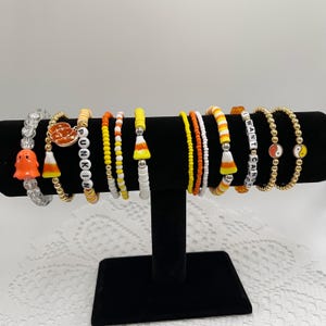 Può includere: Un set di 10 braccialetti a tema Halloween con motivi di mais dolce, zucche, fantasmi e la frase "I want candy".