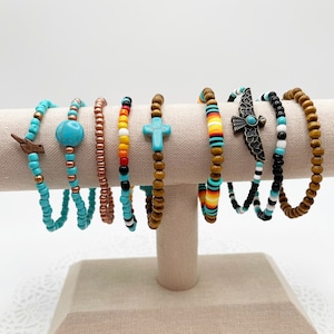 May include: A set of eight beaded bracelets with various colours and patterns, including turquoise, brown, black, white, red, yellow, and orange. Some bracelets feature charms, such as a cross, a bird, and a turquoise stone.