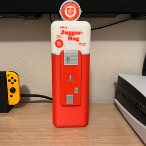 May include: A red and white 3D printed replica of a vintage soda dispenser with the words "Drink Jugger-Nog" and "10c" on the front. The dispenser has a silver top with a red and white logo.