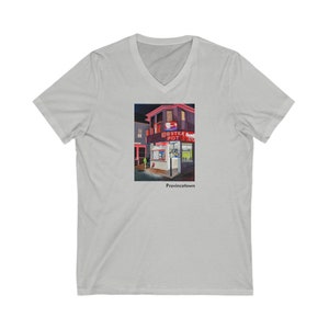 May include: A grey V-neck t-shirt featuring a colourful illustration of a building with a red sign that reads "Lobster Pot" in white lettering. The text "Provincetown" is printed beneath the illustration.