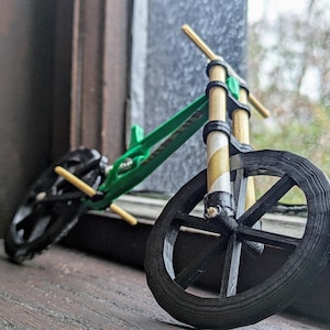 May include: A miniature green and black bicycle with wooden handlebars and wheels. The bicycle is sitting on a wooden surface.