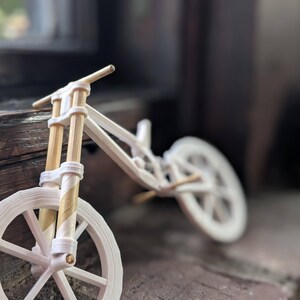Puede incluir: Una bicicleta de juguete de madera blanca y marr&oacute;n con dos ruedas. La rueda delantera est&aacute; enfocada y la rueda trasera est&aacute; desenfocada.
