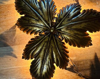May include: A gold-toned metal leaf-shaped wall sconce with a distressed finish. The sconce has a chain hanging from the bottom.