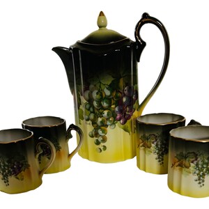 May include: A vintage tea set with a black and yellow teapot and four cups. The teapot and cups are decorated with a grapevine design and have gold accents.
