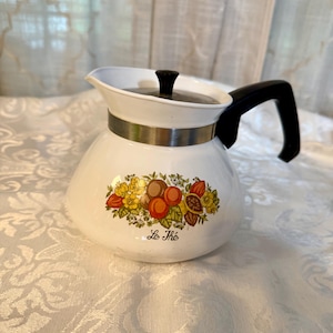 May include: White ceramic teapot with a black handle and lid. The teapot features a decorative band and a colorful fruit and floral design. The text "Le Thé" is printed on the front.