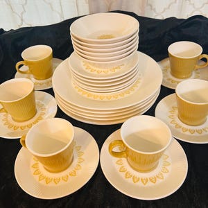 May include: A vintage dinnerware set featuring cream-colored plates, bowls, saucers, and cups. The plates and saucers have a decorative yellow heart pattern around the edges. The cups and bowls are a mustard yellow color.